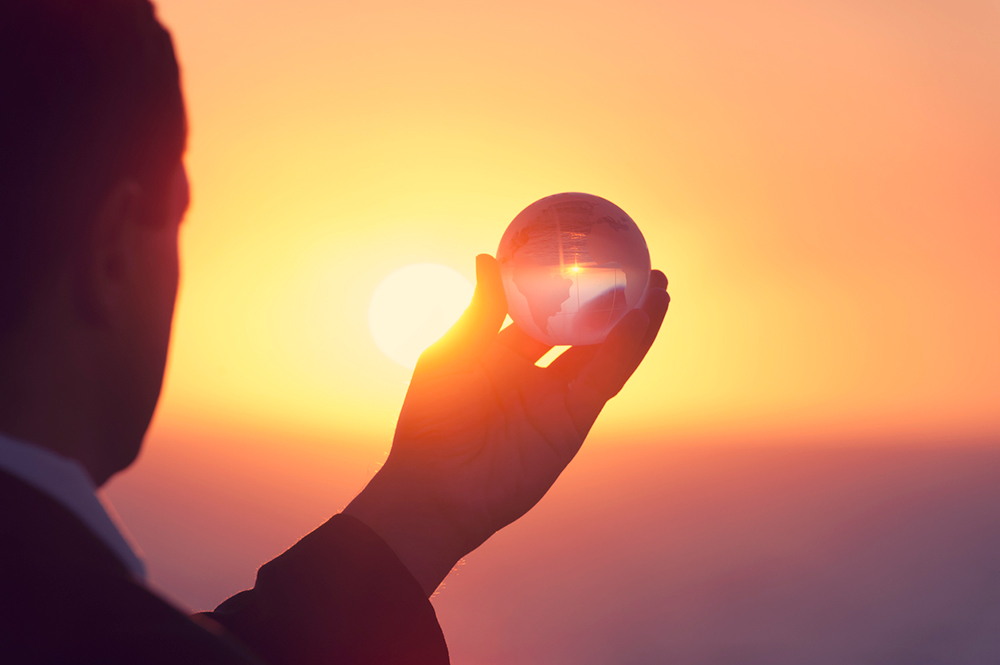 man holding glass globe up against sunset